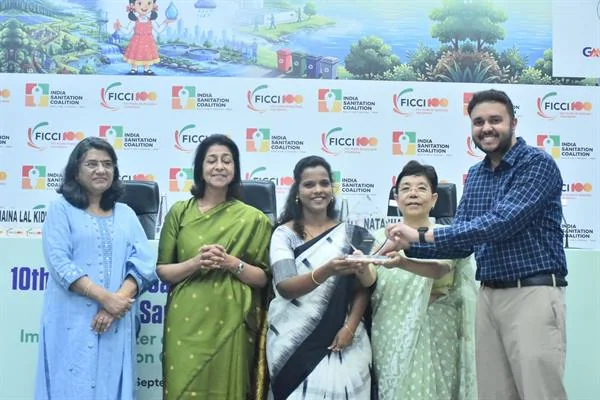 मंच पर चार महिलाएं और एक पुरुष पुरस्कार की ट्रॉफी सौंपते हुए, पीछे ISC-FICCI और इंडिया सैनिटेशन कोएलिशन के लोगो वाला पटल