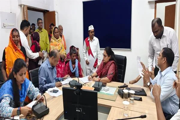 बैठक कक्ष में मेज के दोनों ओर बैठे अधिकारी और आवेदन लेकर खड़े ग्रामीण